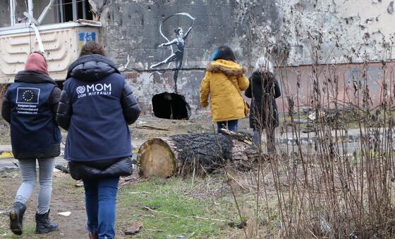 Сотрудники МОМ проходят мимо разрушенного войной здания с граффити балерины в Киевской области.